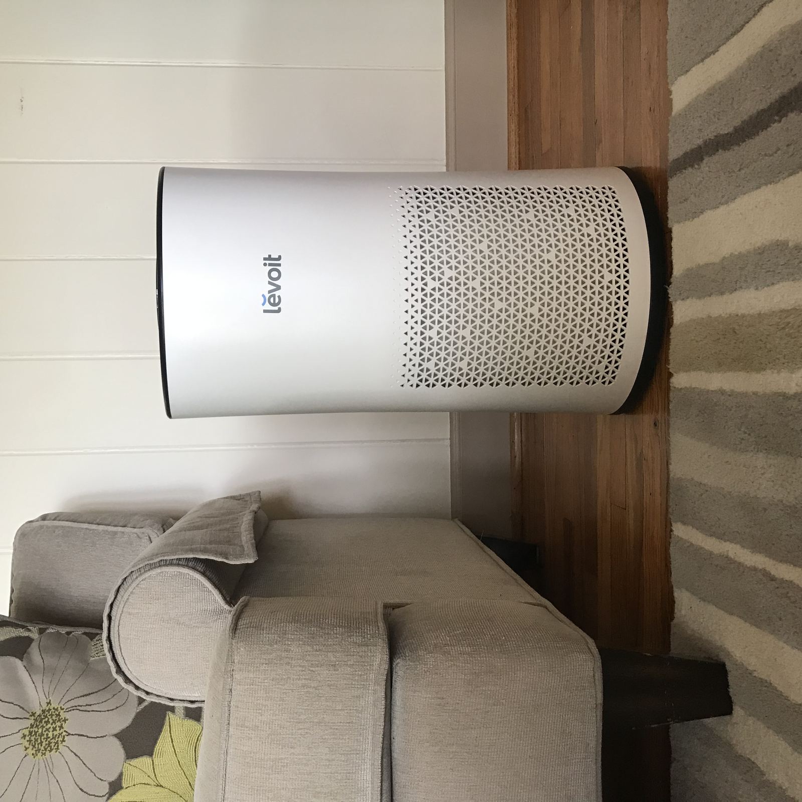 A white tower air purifier standing on a wooden floor beside a sofa