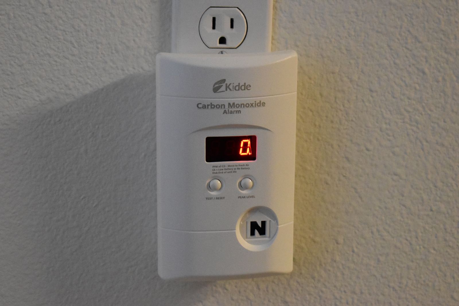 A plug-in carbon monoxide alarm with a digital display on a wall outlet