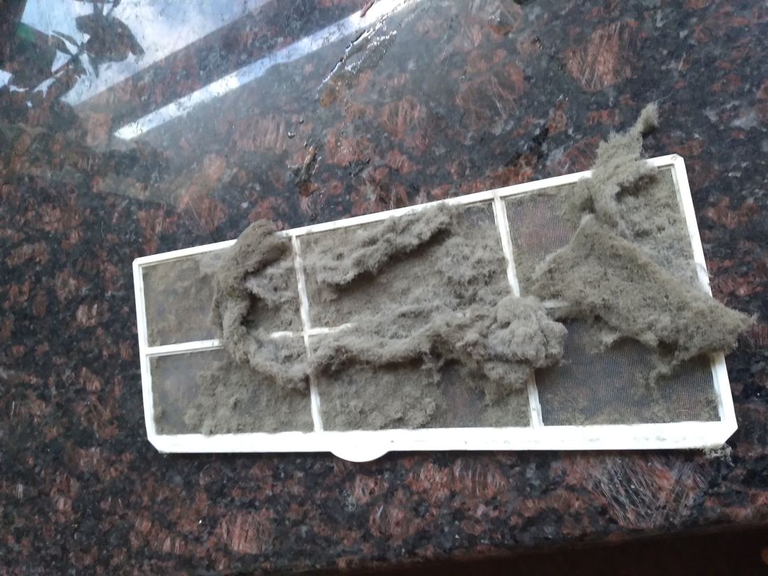 A removed air conditioner filter covered in grey dust