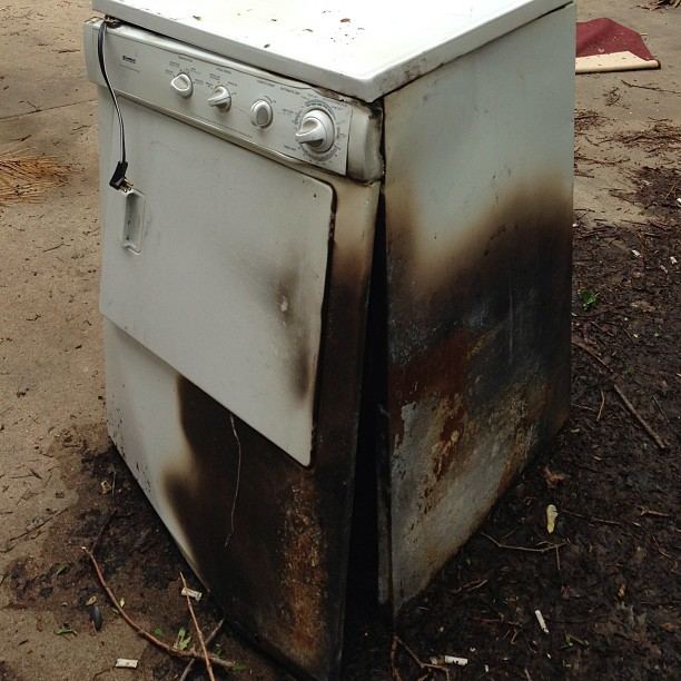 A clothes dryer with burn and smoke damage on its side