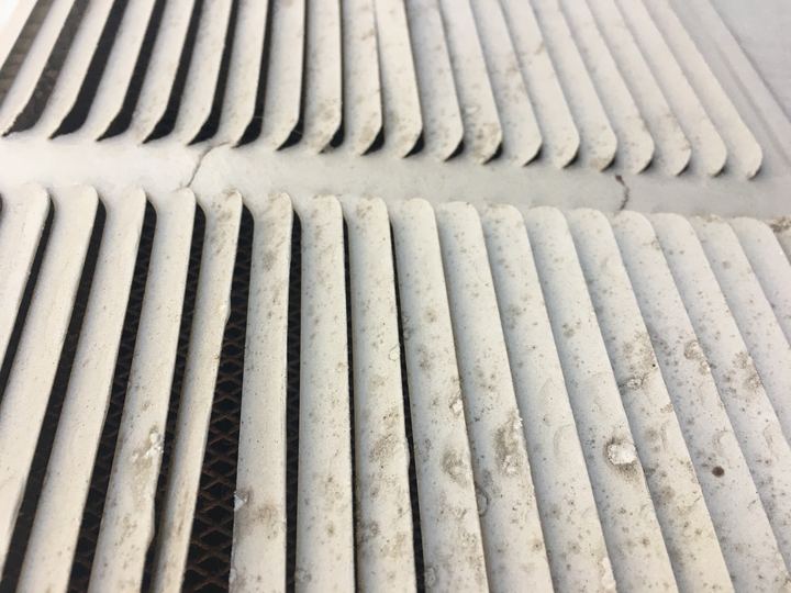Close-up of a dusty air vent with grey dust on its louvers