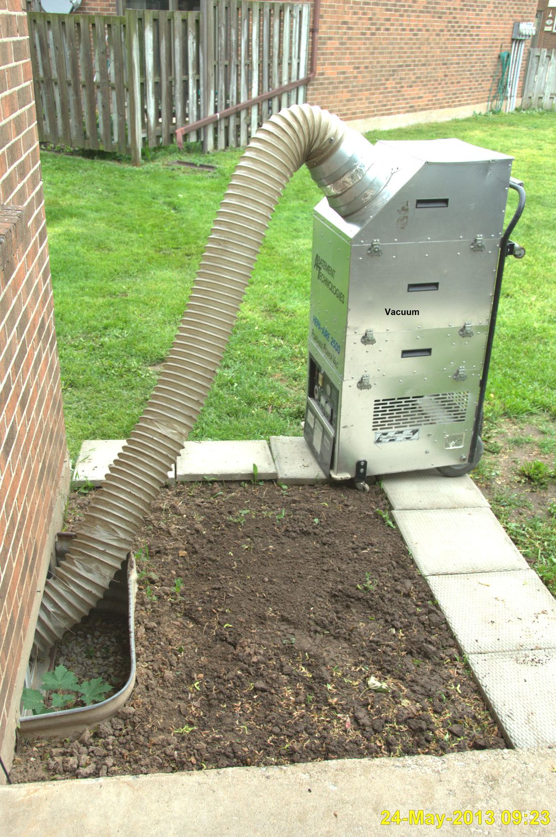 A portable vacuum collection unit outside a house with a large hose running inside