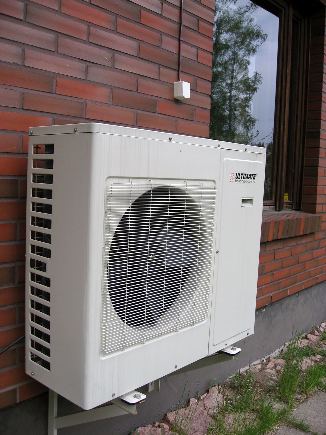 A compact outdoor heat pump unit mounted on a brick wall