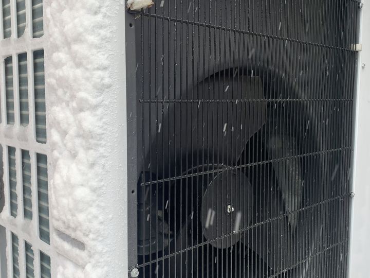 An air-source heat pump outdoor unit with snow falling around it