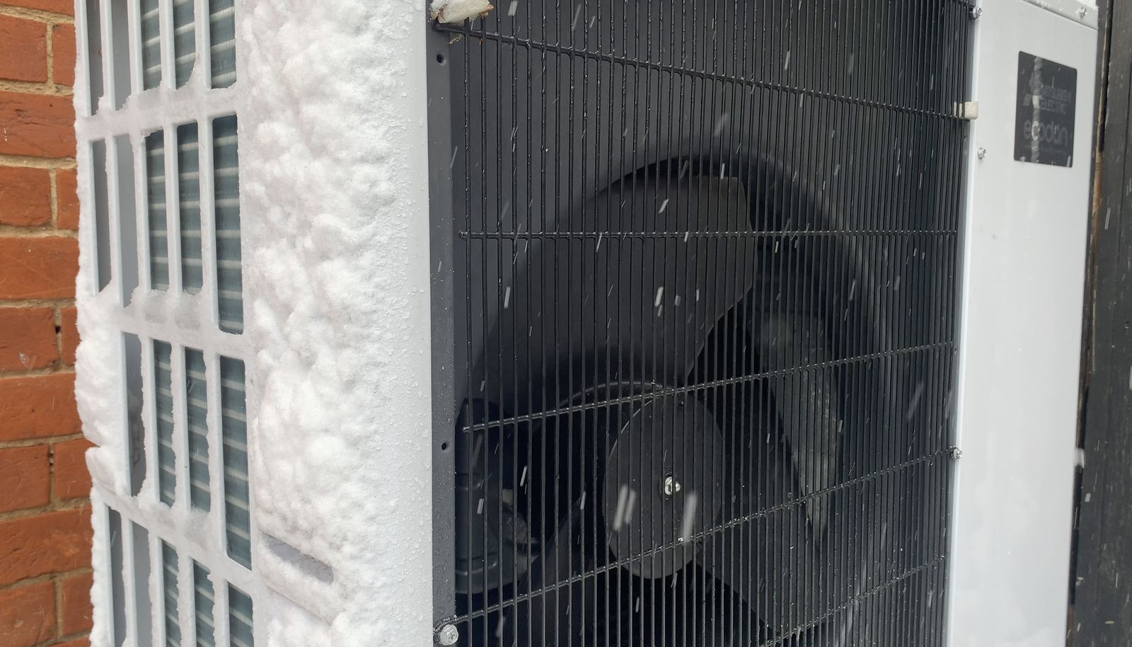 An air-source heat pump outdoor unit with snow falling around it