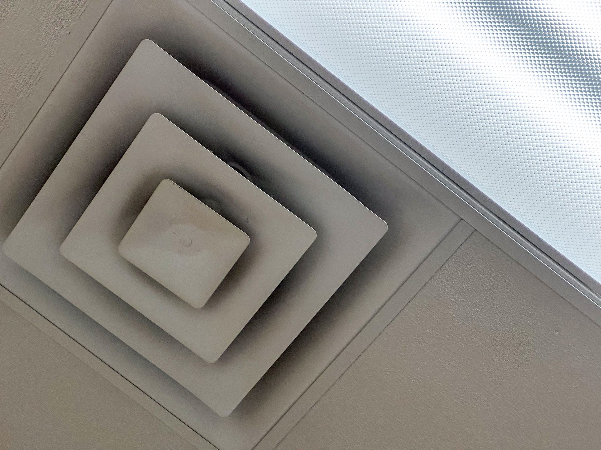 A square ceiling air vent next to a light panel