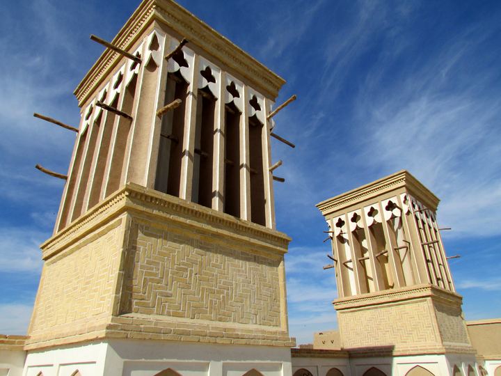 Two tall traditional windcatcher towers against a blue sky in Yazd