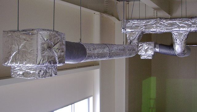 Insulated air ducts wrapped in silver foil running below a ceiling