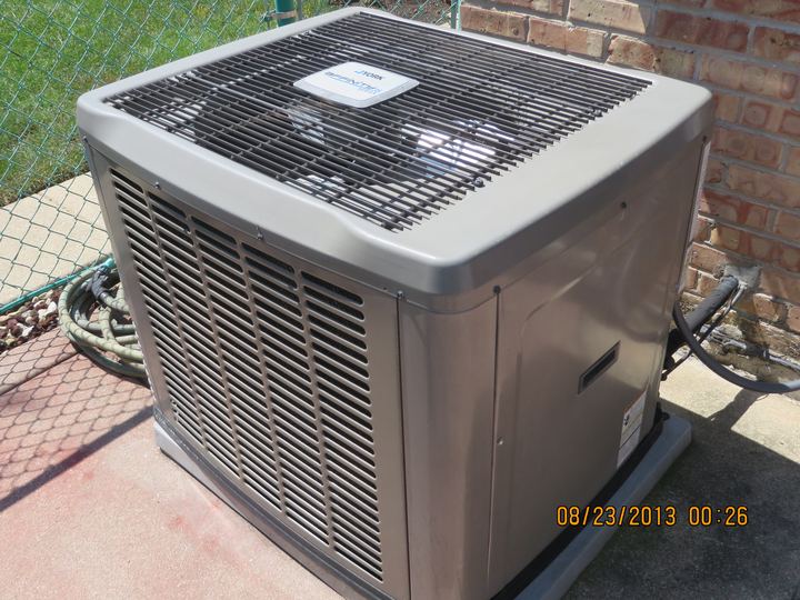 An outdoor condenser unit for a central air conditioner beside a brick house