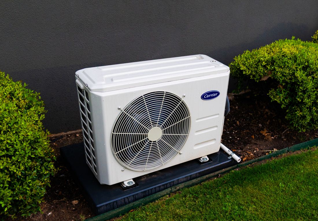 A white outdoor split system unit on a pad surrounded by shrubs